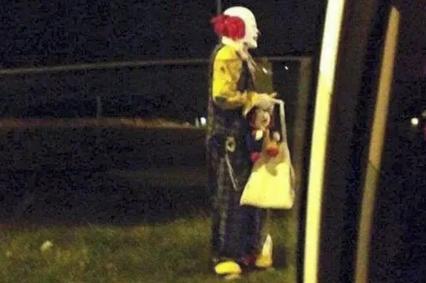 Clown figure standing near a fence at night