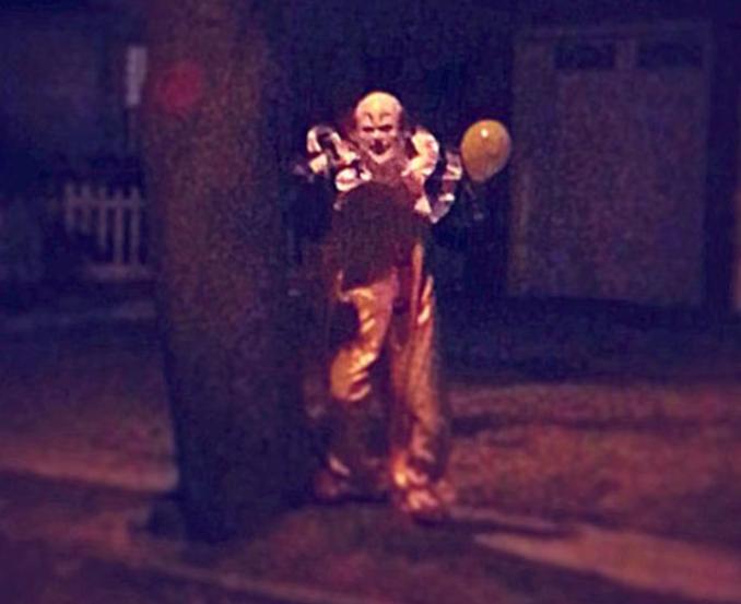 Clown standing at night near a tree